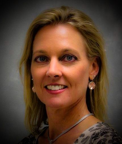Kathy wearing a necklace and earrings is smiling for the camera.