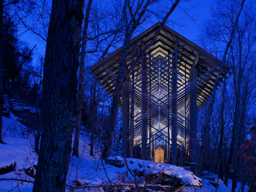 A small building in the middle of a snowy forest at night.
