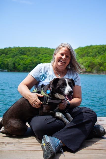 Toni is sitting on a dock holding a dog.