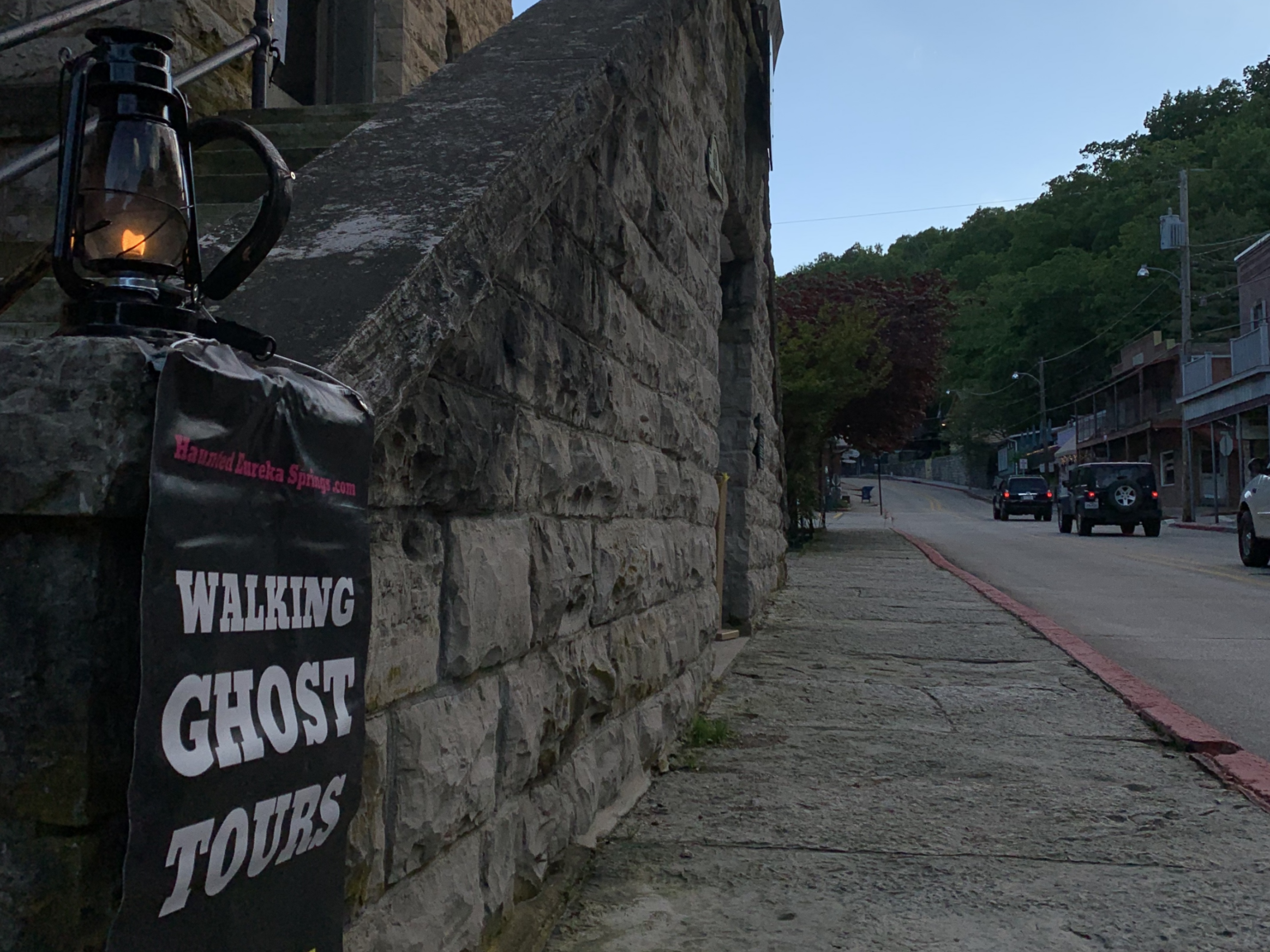 A sign for walking ghost tours is hanging on a brick wall.