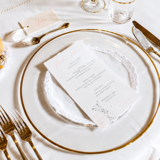 Elegante apparecchiatura da tavola bianca e oro con menù su un piatto, pronta per un evento formale.