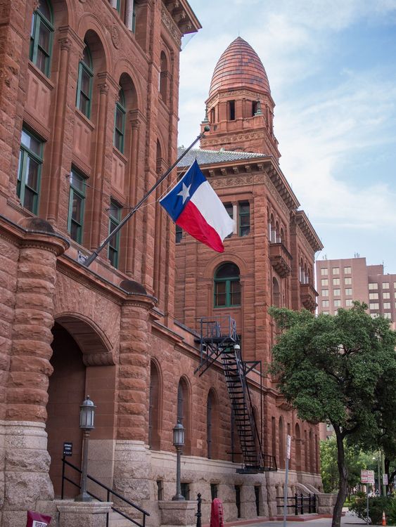A texas flag is flying in front of a large brick building