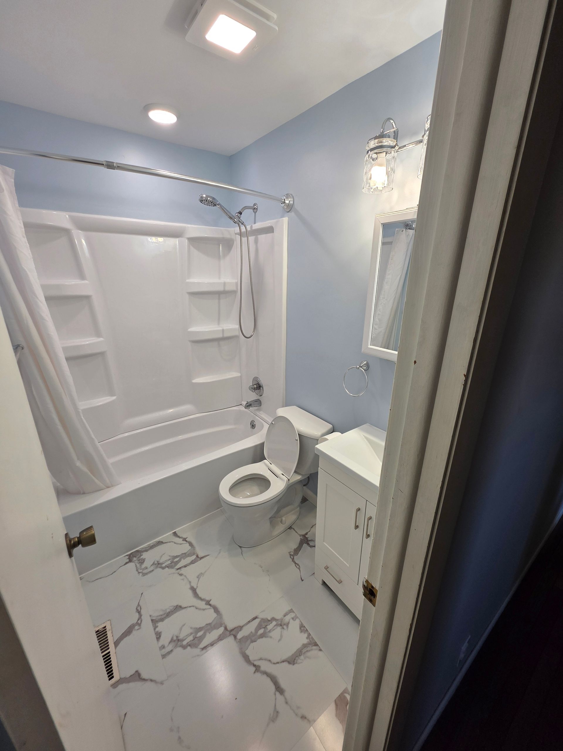 Bathroom with white tub, toilet, vanity, marble floors, and light blue walls. | Urbana, IL