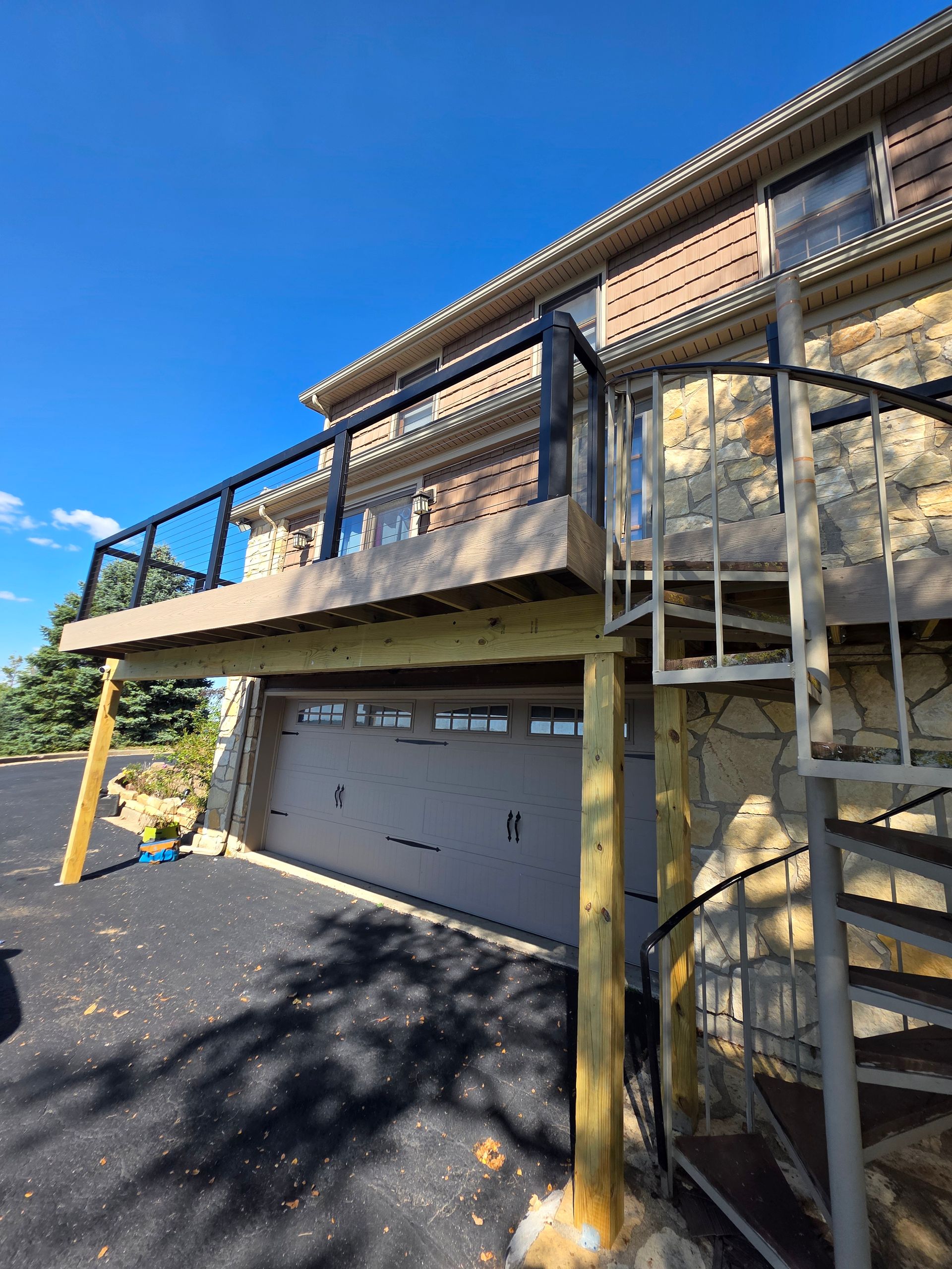 A wooden deck built above a garage door, featuring a black railing and a metal spiral staircase against a stone house wall - Danville, IL