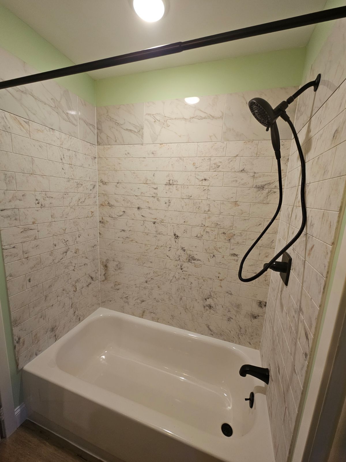 Bathtub with white marble-like tile walls and black shower head and rod, in a bathroom. | Urbana, IL
