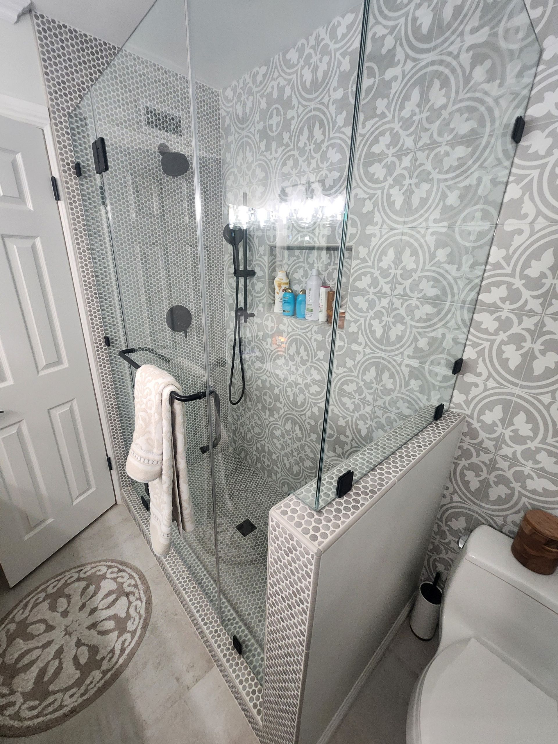 Modern bathroom with patterned tile shower, glass doors, and white walls. | Urbana, IL