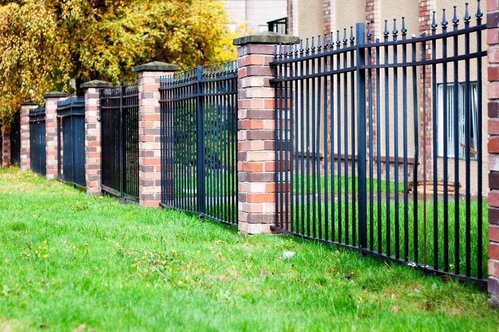 Wrought iron fence with brick pillars and green grass.