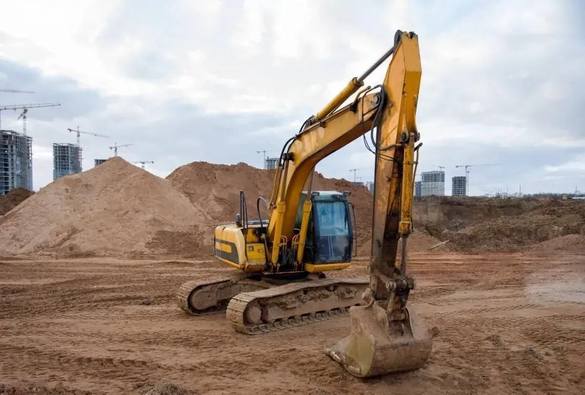 Yellow excavator on a dirt construction site with soil piles and an overcast sky
