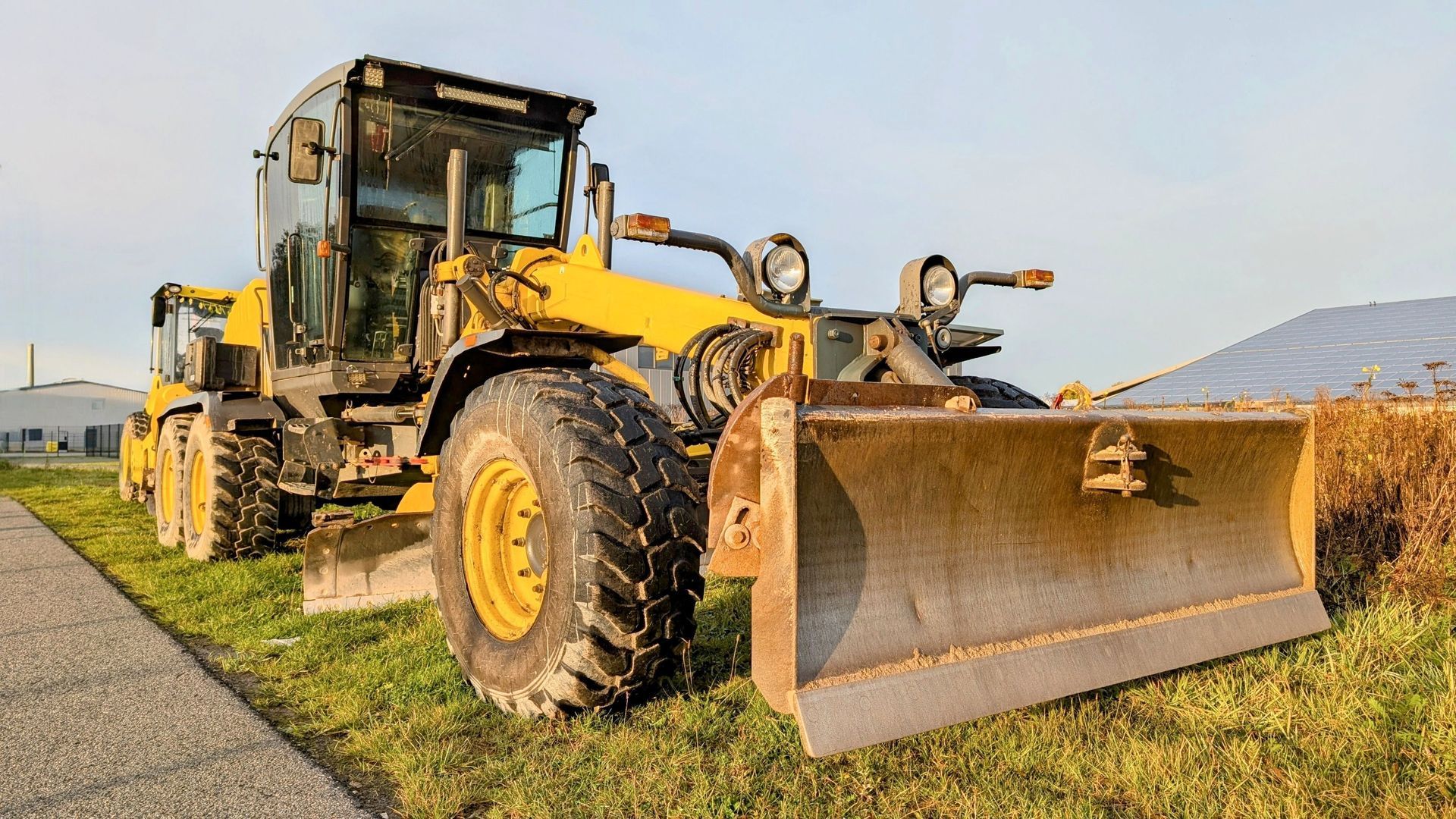 Yellow bulldozer with a wide blade parked on grass in a field, with another machine behind it.