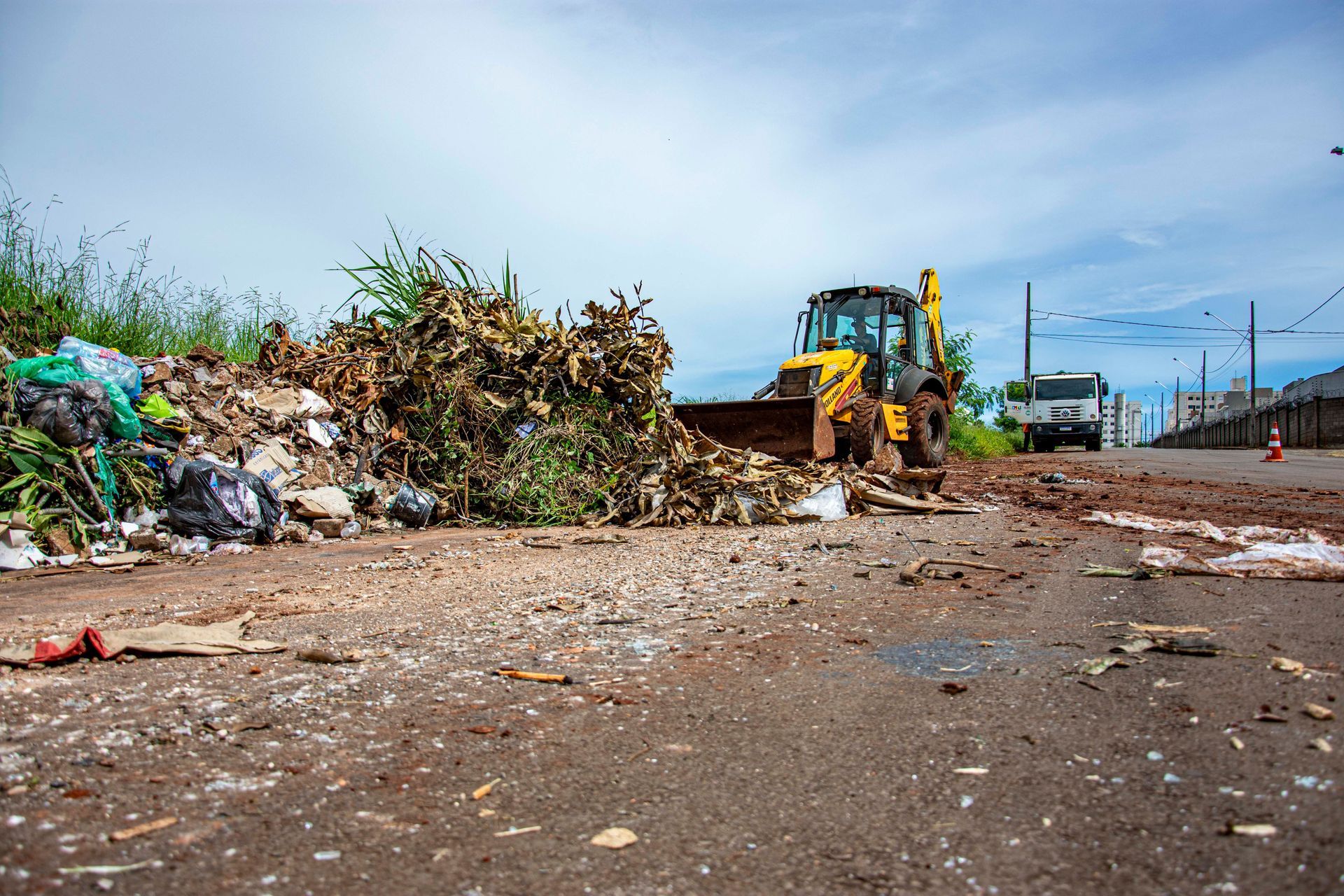 Bulldozer clearing a roadside垃圾 pile under a cloudy sky, with debris scattered across the ground.