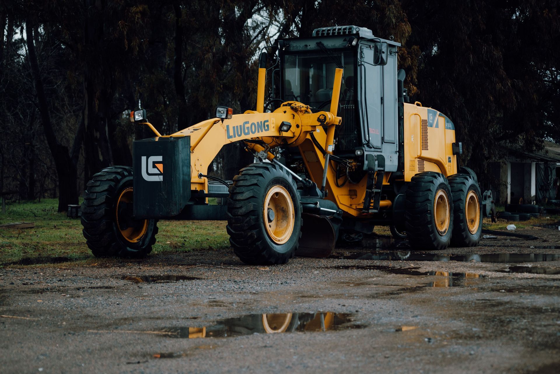 Yellow wheel loader parked on wet pavement in a dark wooded area