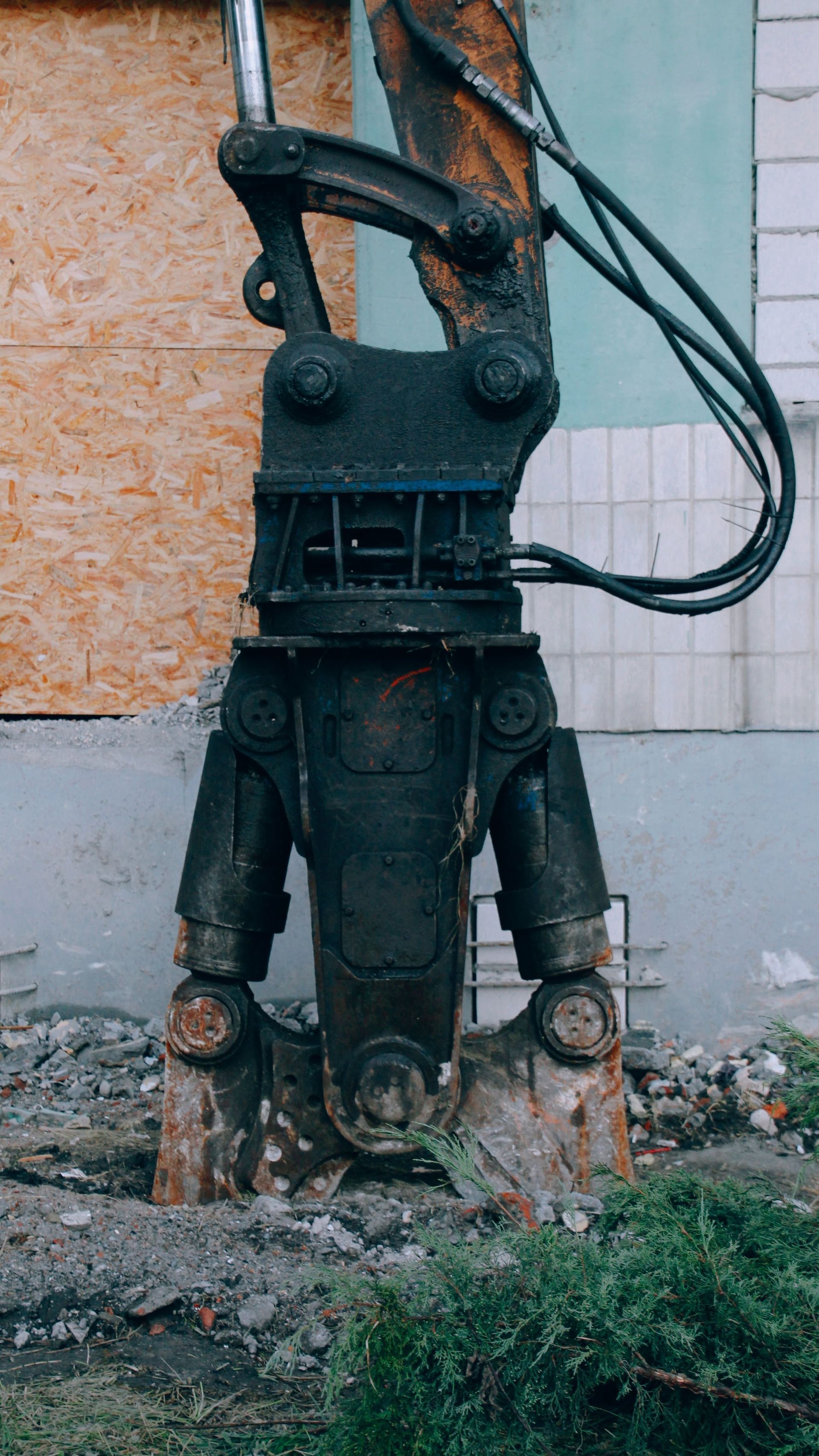 Rusty industrial machine part with cables and pipes, standing on a damaged concrete surface against a wall.