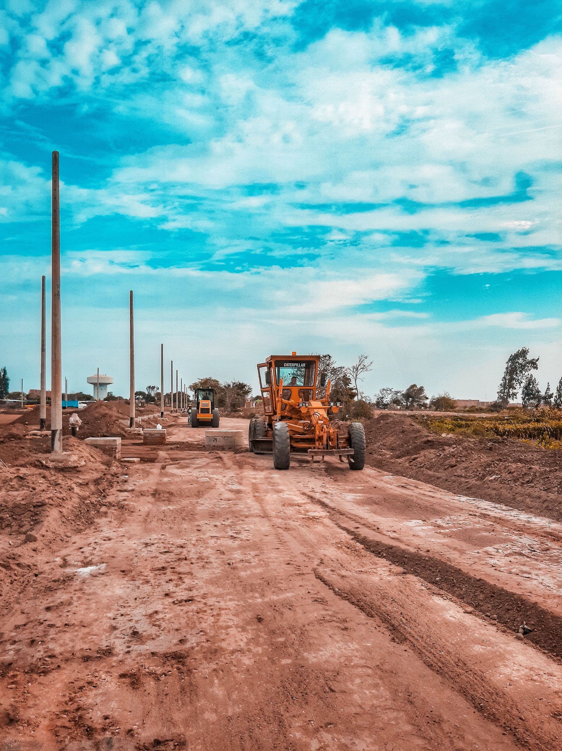 Road construction site with a bulldozer on a muddy dirt road under a bright blue sky