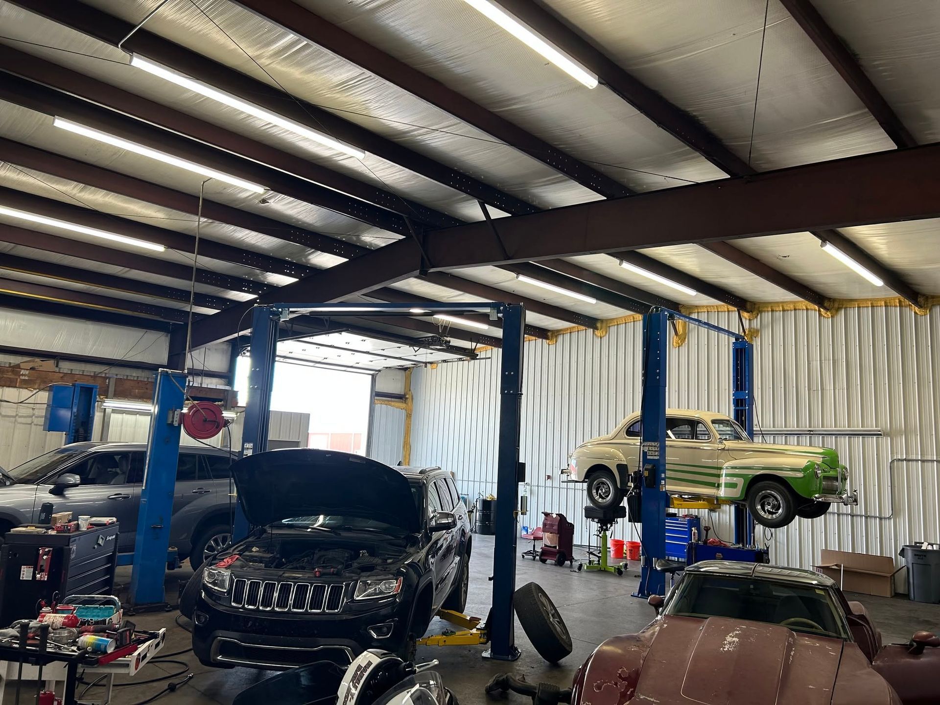 Auto repair garage with several cars on lifts and a green classic car on a hoist under a metal roof| Sonny's Automotive Repair and Sales