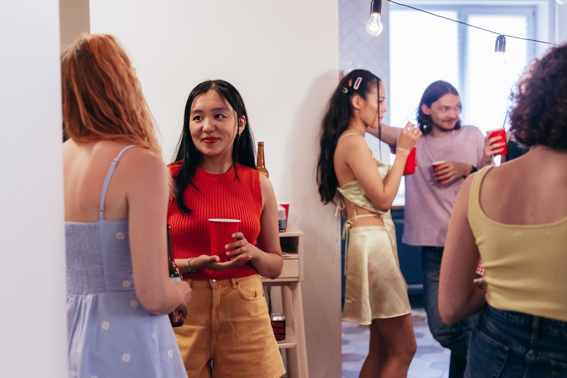 People chatting and holding drinks at a casual indoor gathering in a bright room