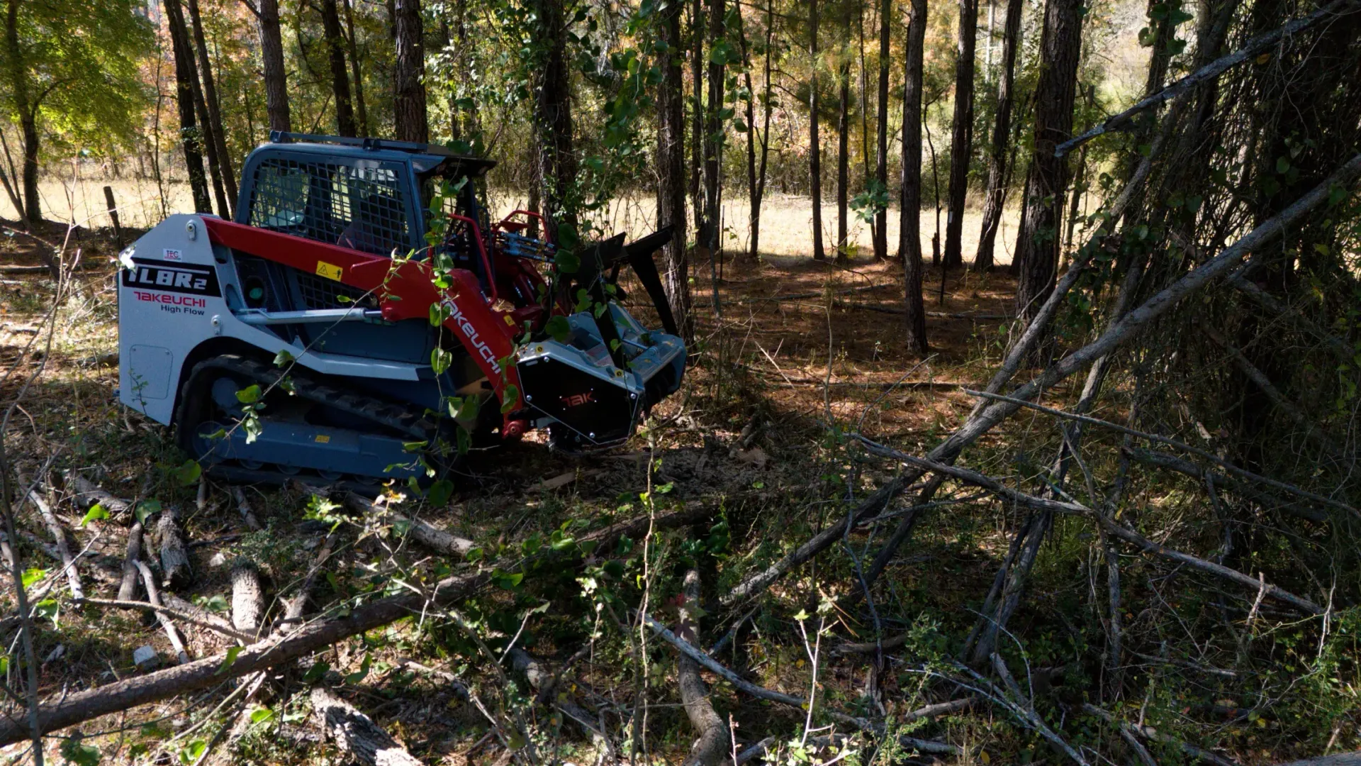Small blue utility vehicle damaged in a wooded area with broken branches around it.