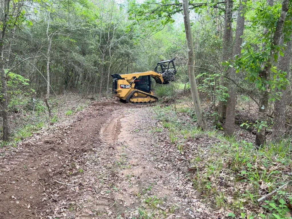 Yellow forestry machine clearing a dirt path in a wooded area