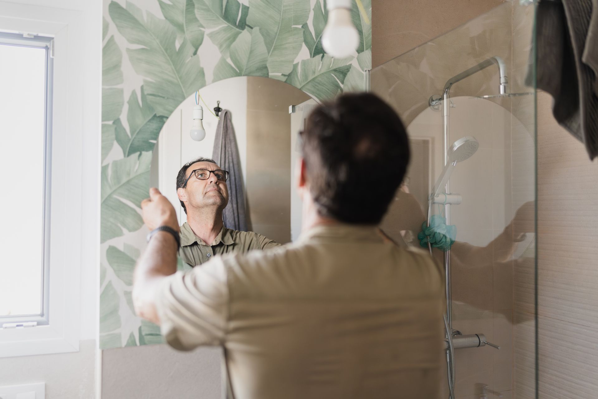 Person pointing at round mirror in bathroom with leafy wallpaper. Person pointing at round mirror in bathroom with leafy wallpaper.