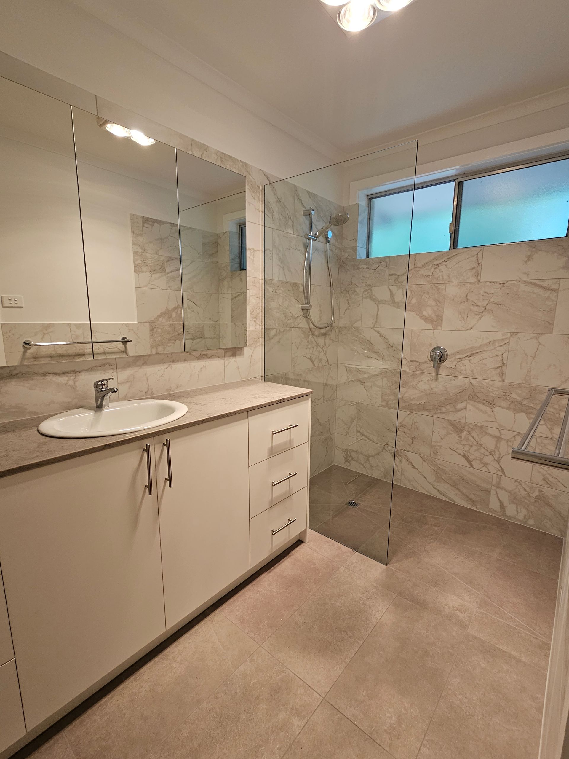A bathroom with a sink , mirror and walk in shower.