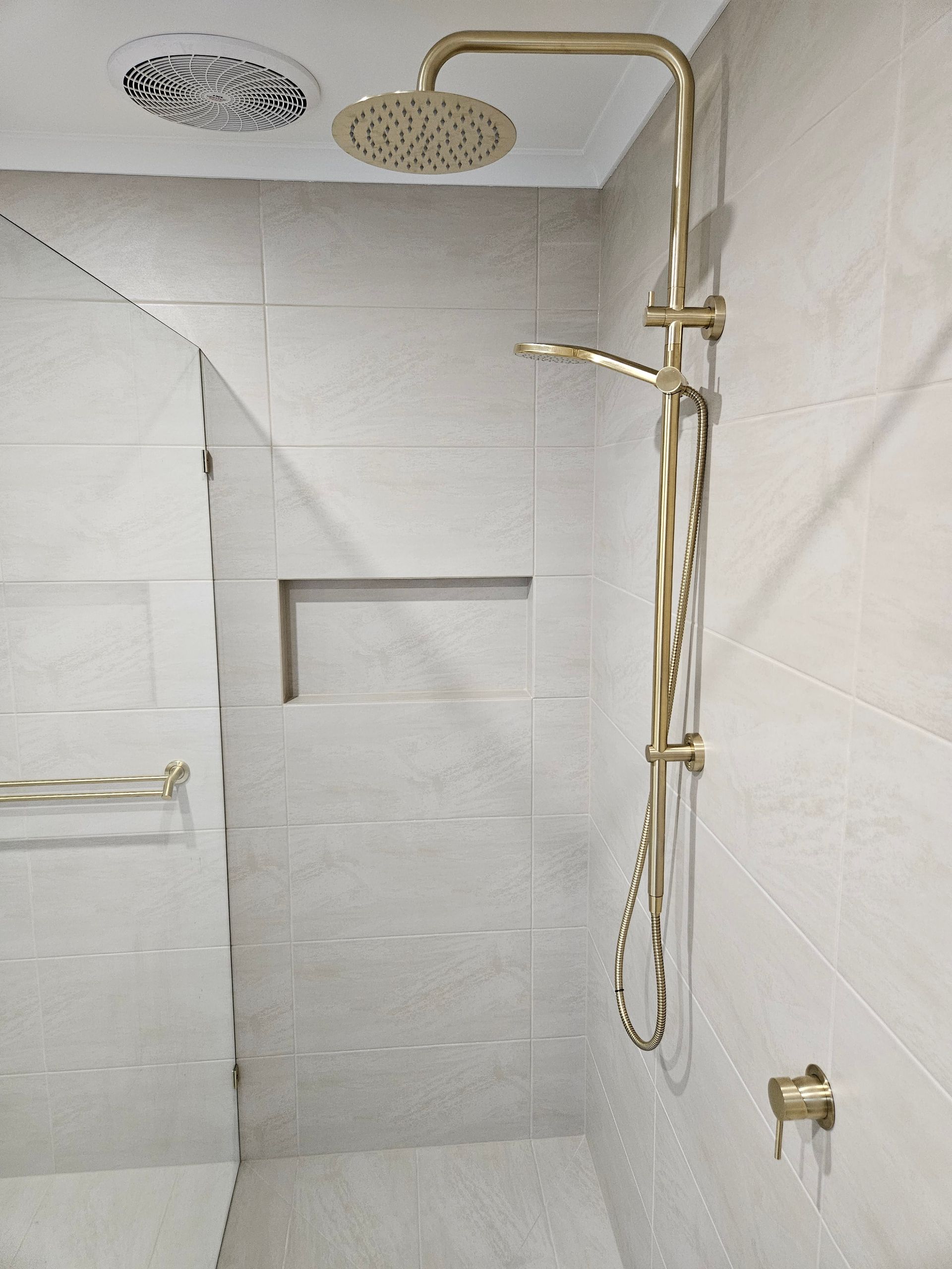 A shower with a brass shower head and a glass door.