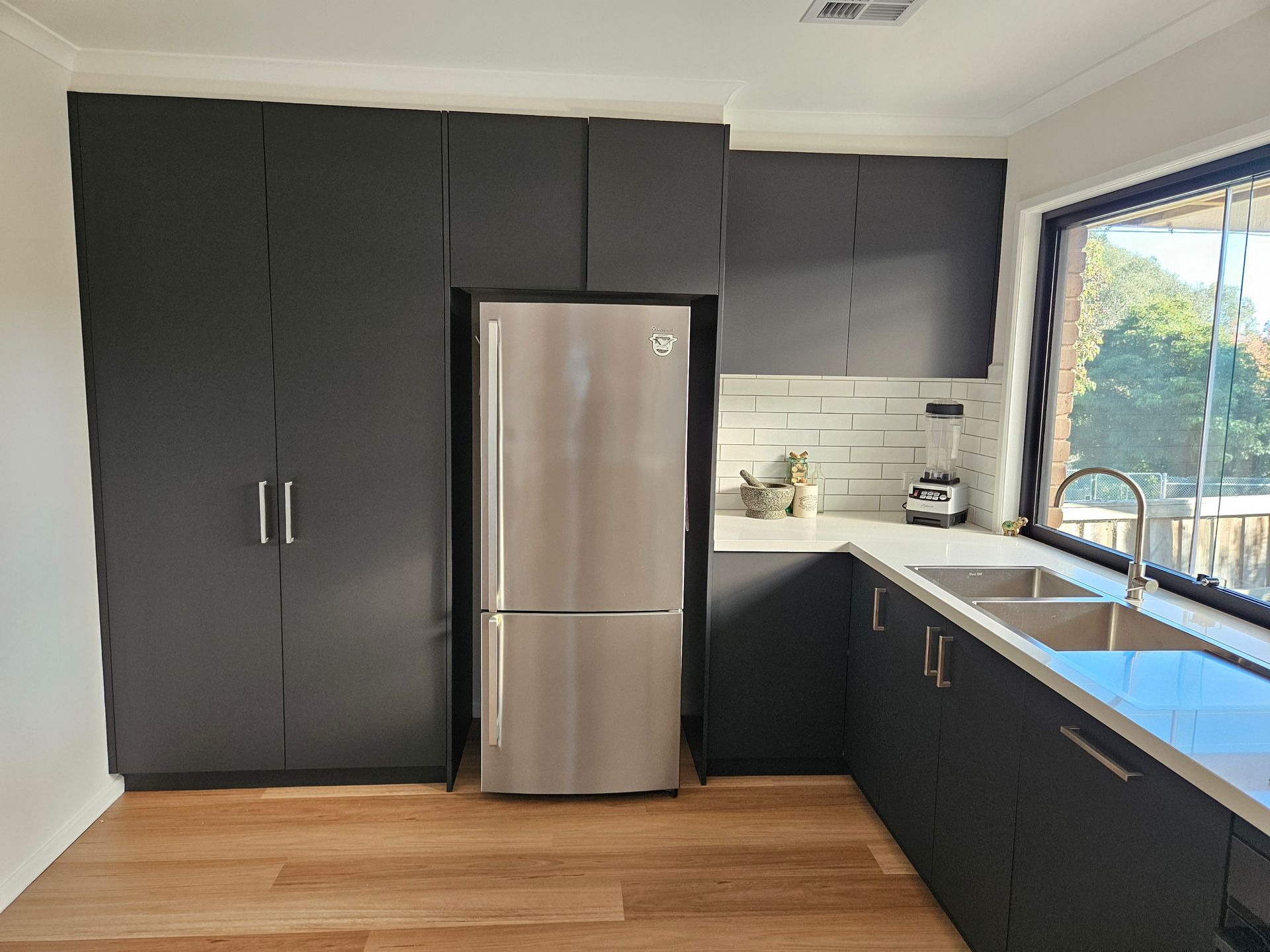 A kitchen with black cabinets and a stainless steel refrigerator