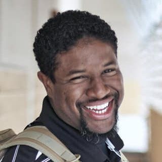 A man with a beard is smiling and wearing a backpack.