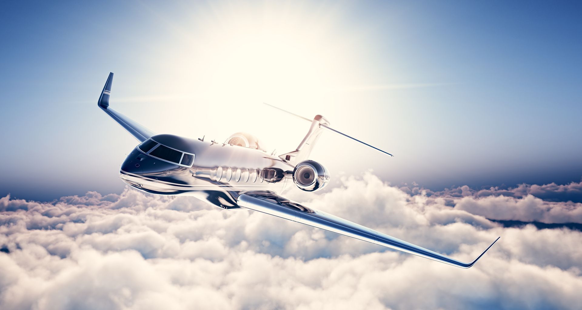 Shiny silver private jet soaring above fluffy white clouds.