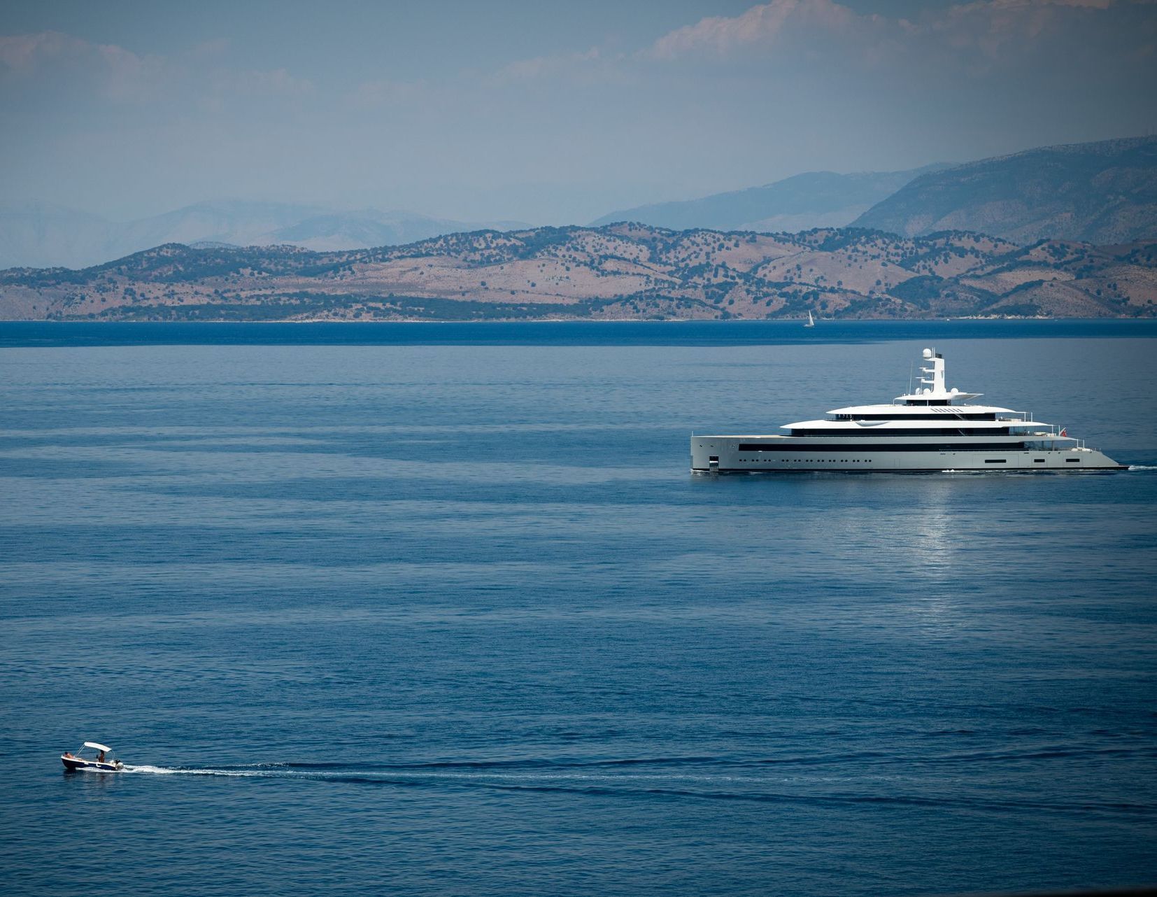 large super modern white superyacht sails across Dassia Bay Corfu with small motorboat in foreground