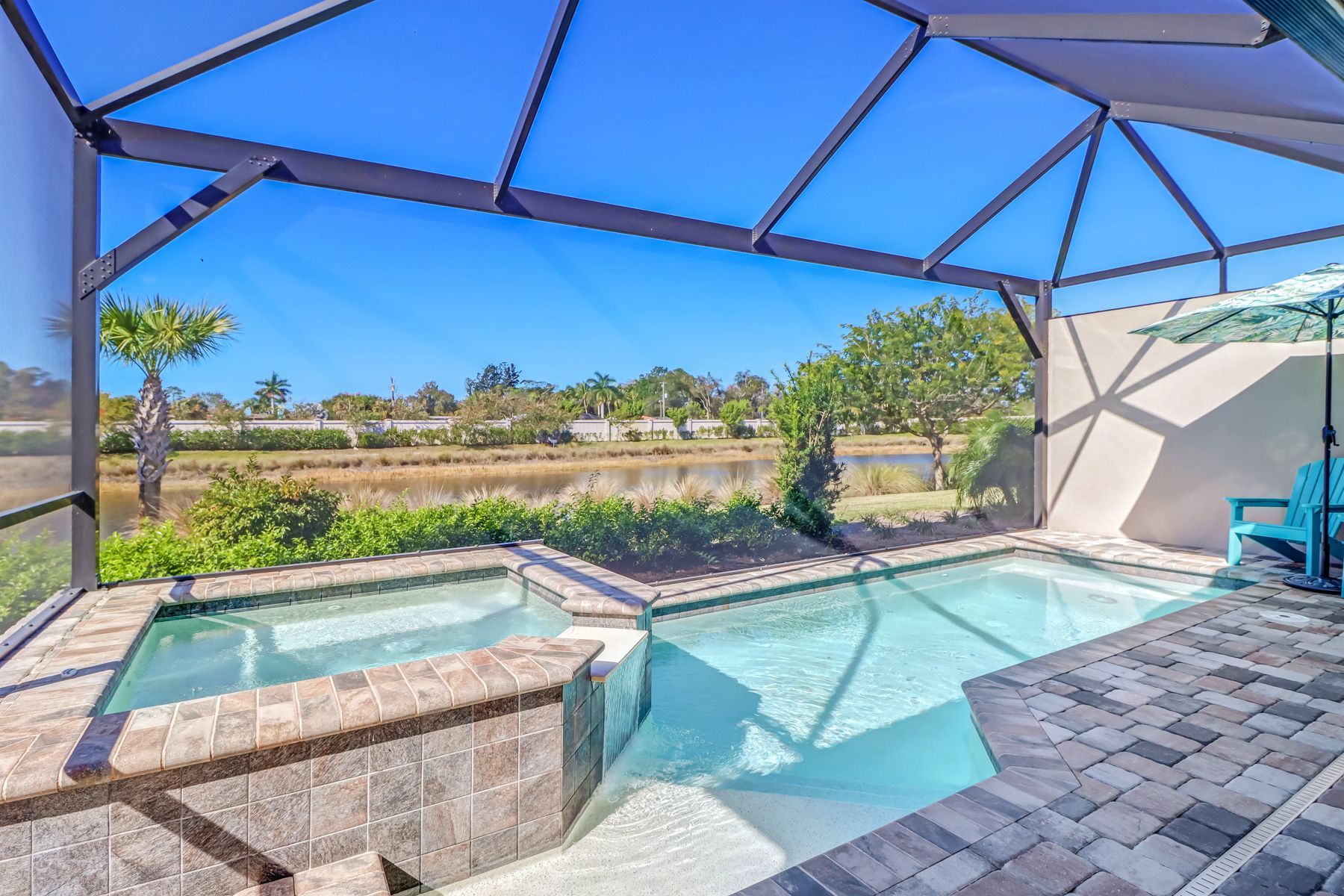 Screened backyard patio with blue pool and hot tub beside stone pavers and desert landscape