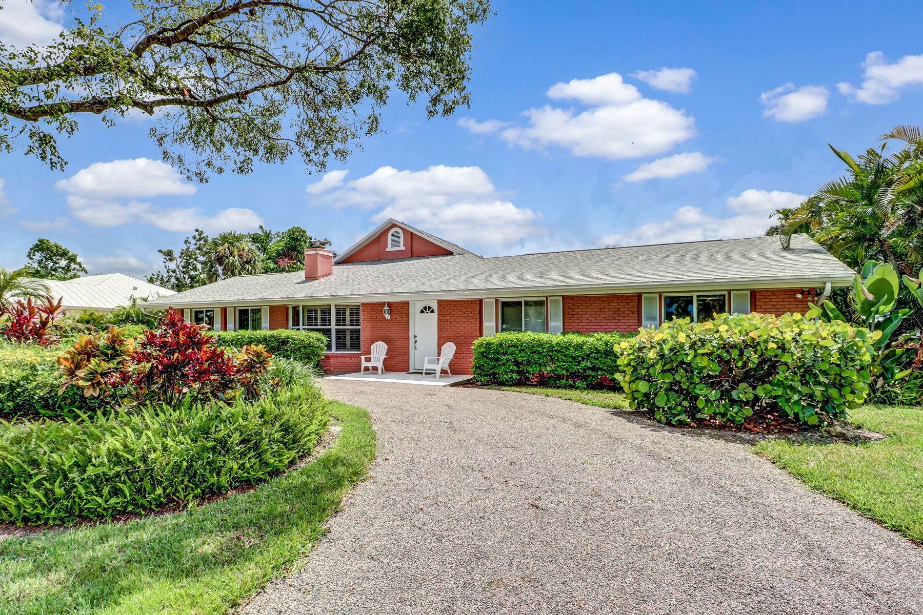 Single-story red brick house with a curved gravel driveway and landscaped front yard