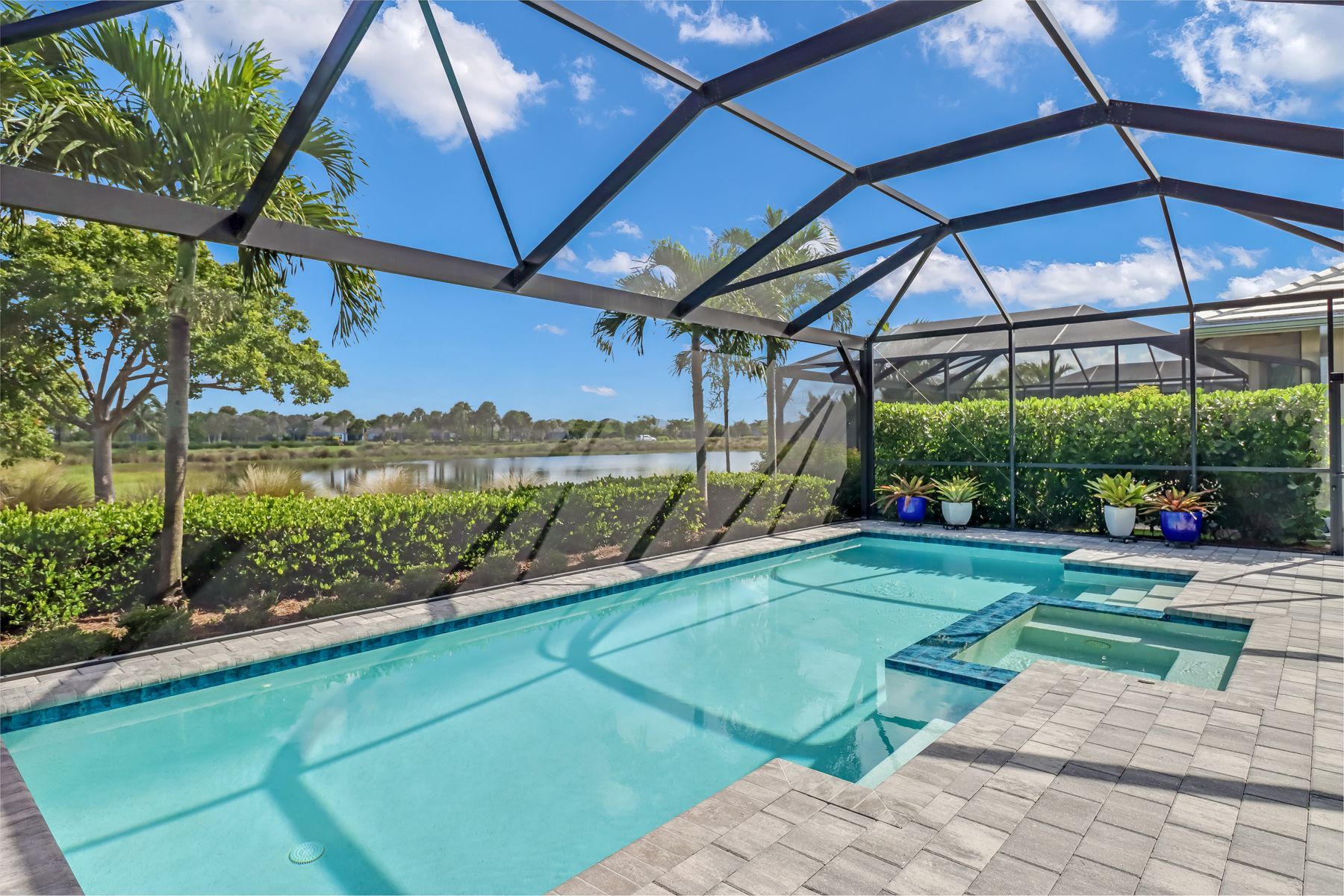 Screened backyard pool with turquoise water, patio pavers, and lake view under a blue sky