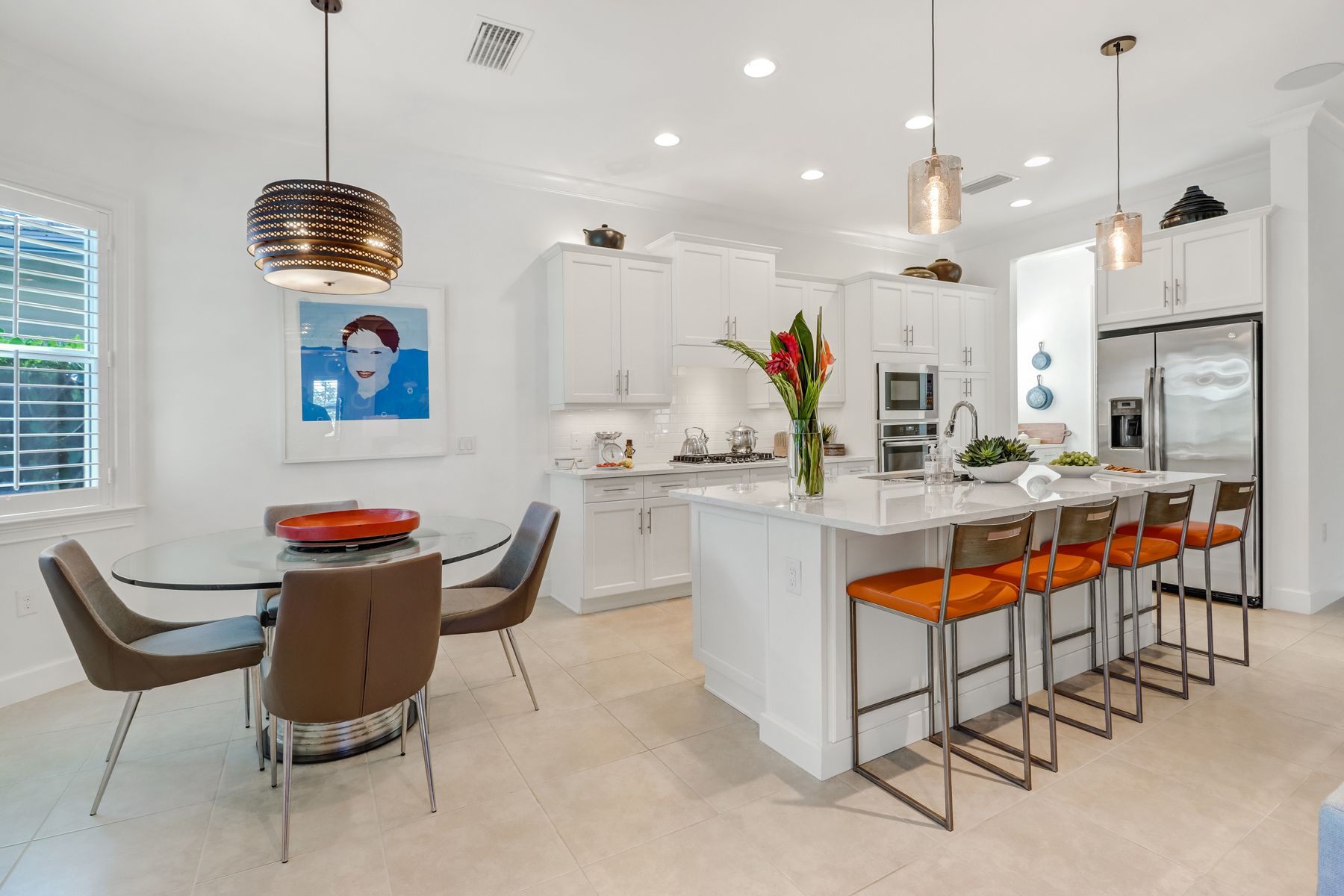 Bright modern kitchen and dining area with white island, orange stools, and a round table by the window.