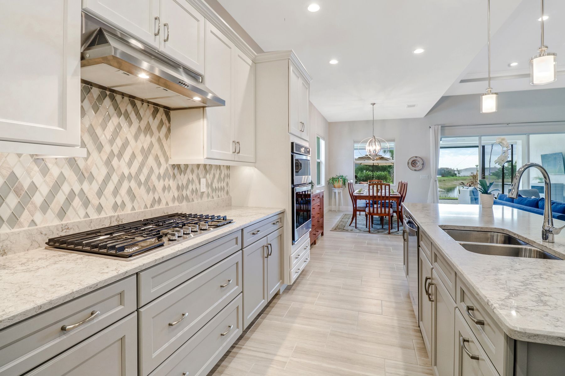 Bright modern kitchen with white cabinets, marble counters, gas stove, and large island leading to a dining area and patio.