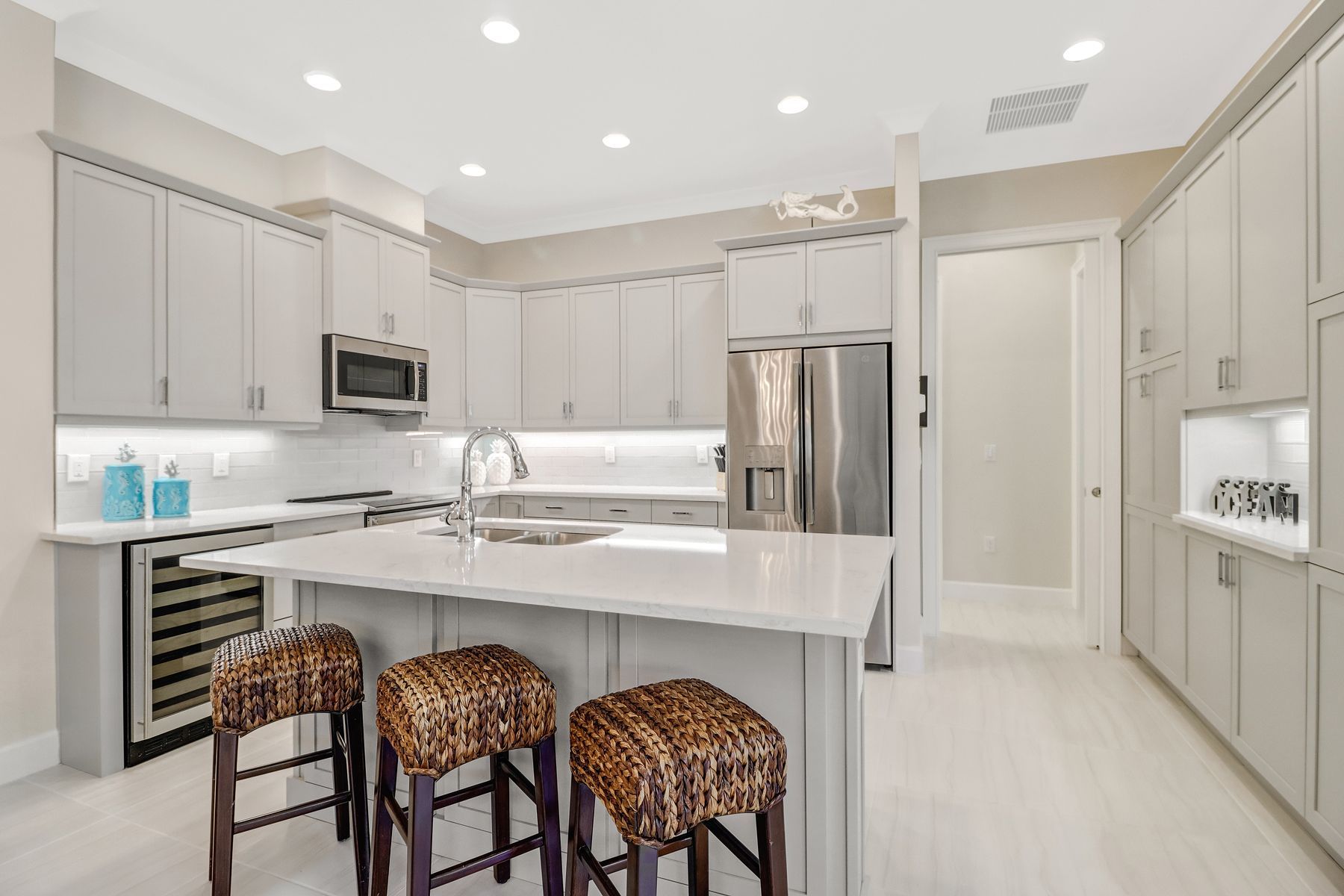 Modern white kitchen with gray cabinets, stainless appliances, island, and three patterned stools
