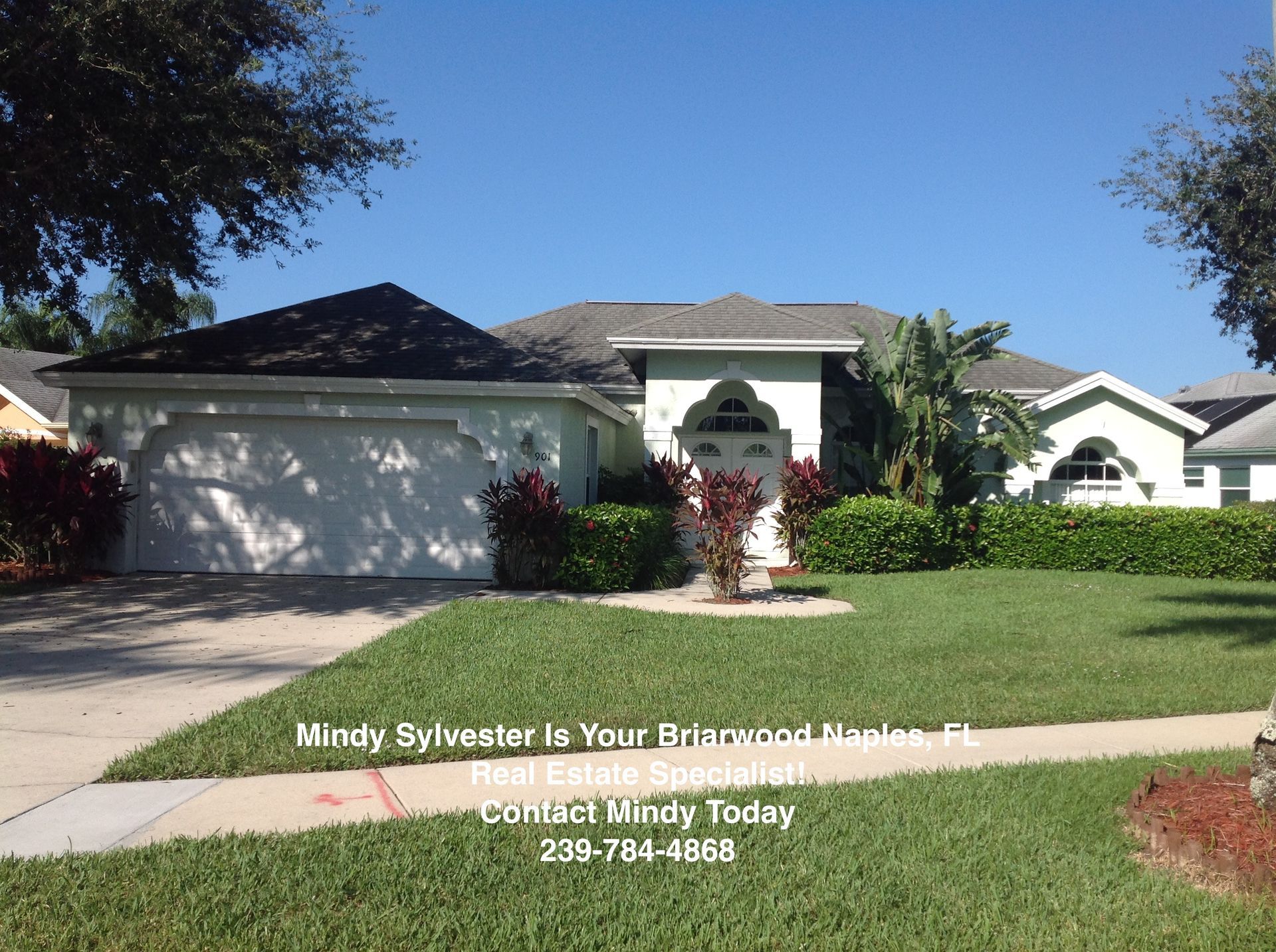 Suburban house with white garage and green lawn under a clear blue sky, with real estate text overlay