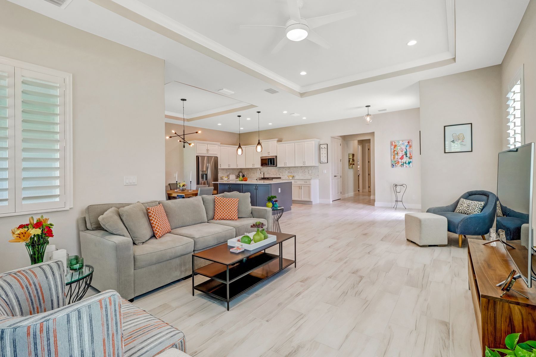 Bright open living room with gray sofa, blue chair, coffee table, and kitchen in background