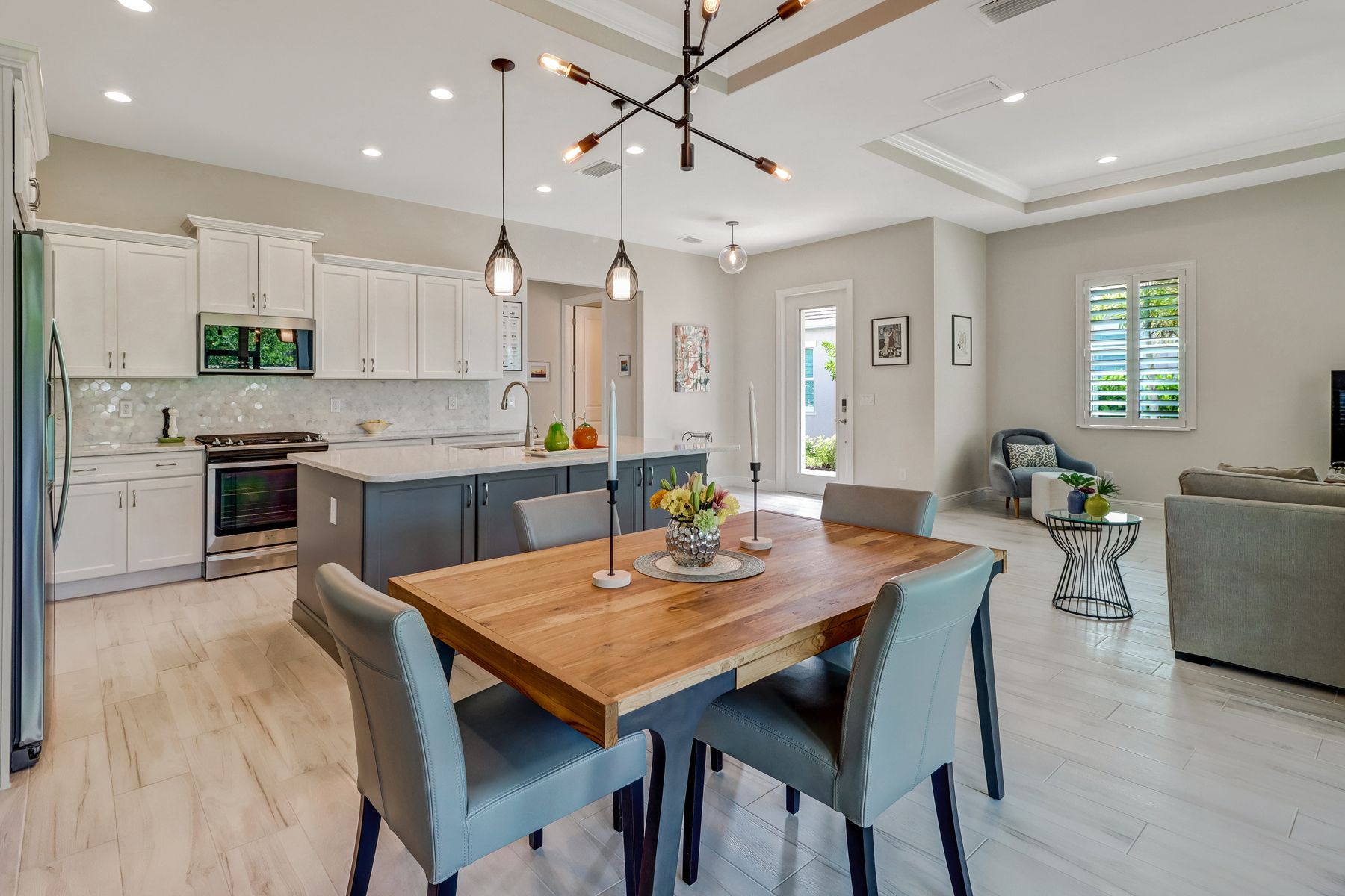 Bright open kitchen and dining area with white cabinets, wooden table, gray chairs, and pendant lights.