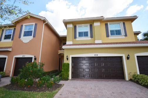 Two-story suburban townhouses, one yellow and one orange, with a garage and driveway under a blue sky