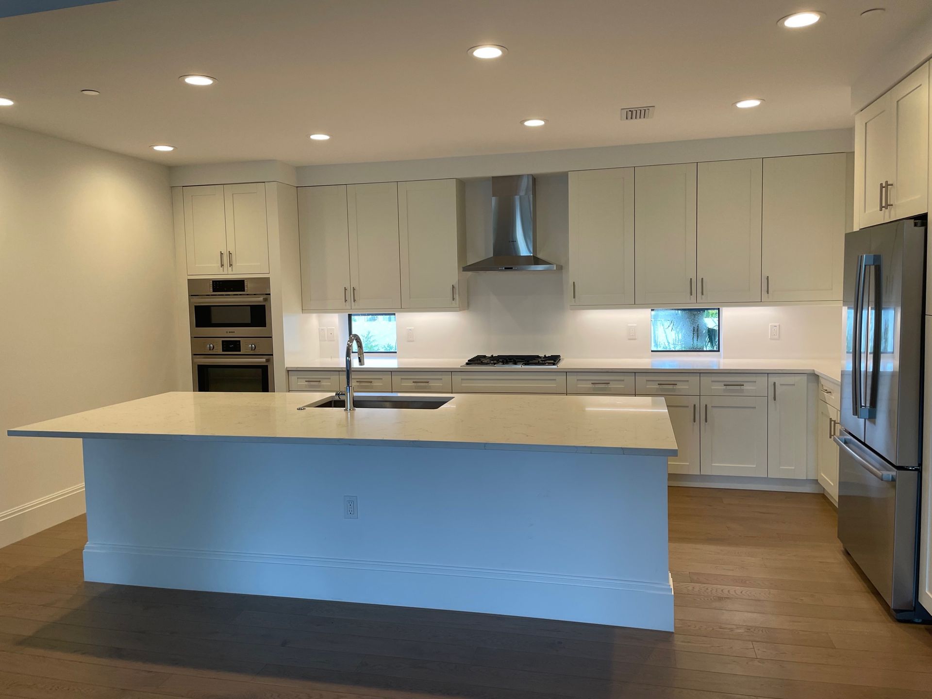 Modern white kitchen with large island, stainless steel appliances, and hardwood floors