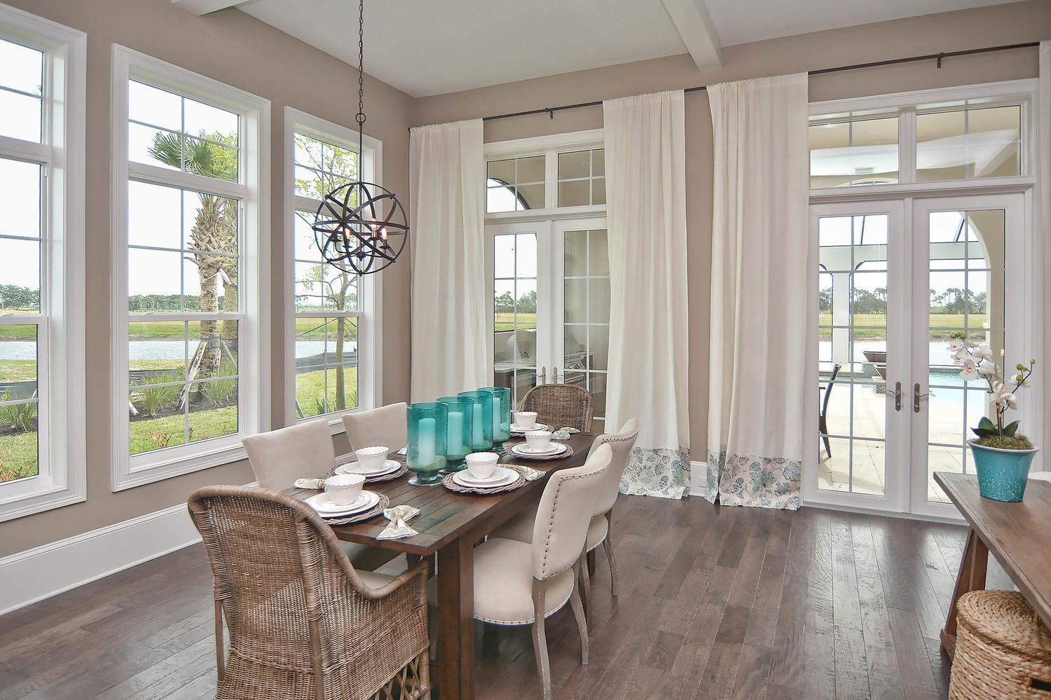 Bright dining room with large windows, a long table, woven chairs, and a dark wood floor.