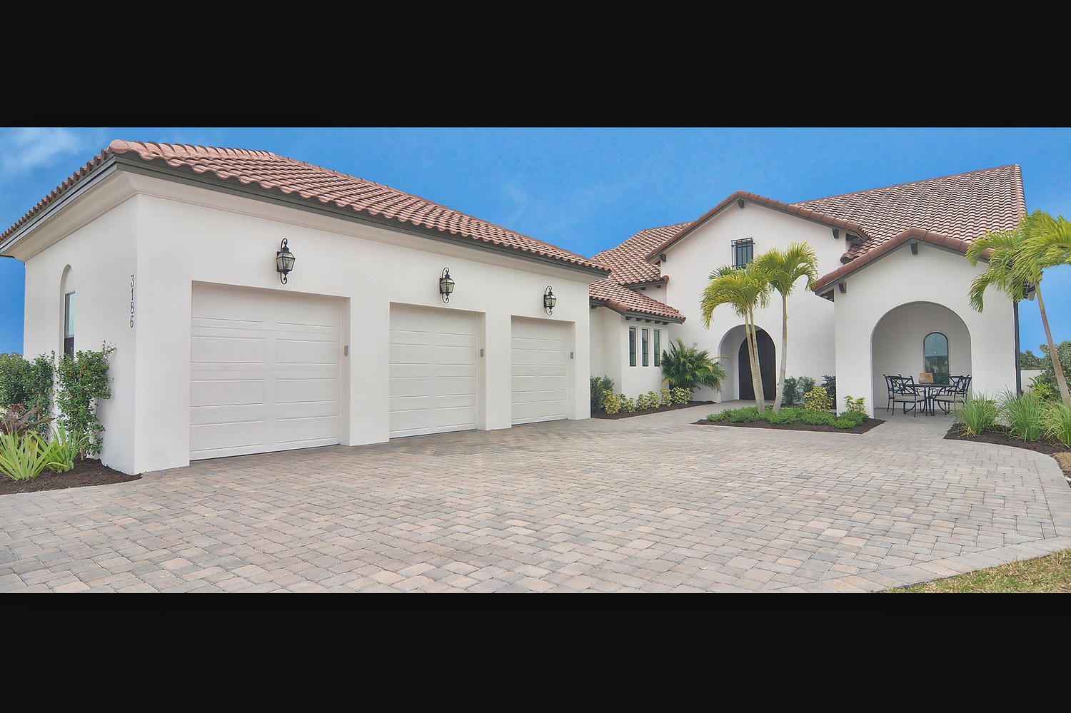 Luxury white stucco house with red tile roof, double garage, and palm trees on a cobblestone driveway