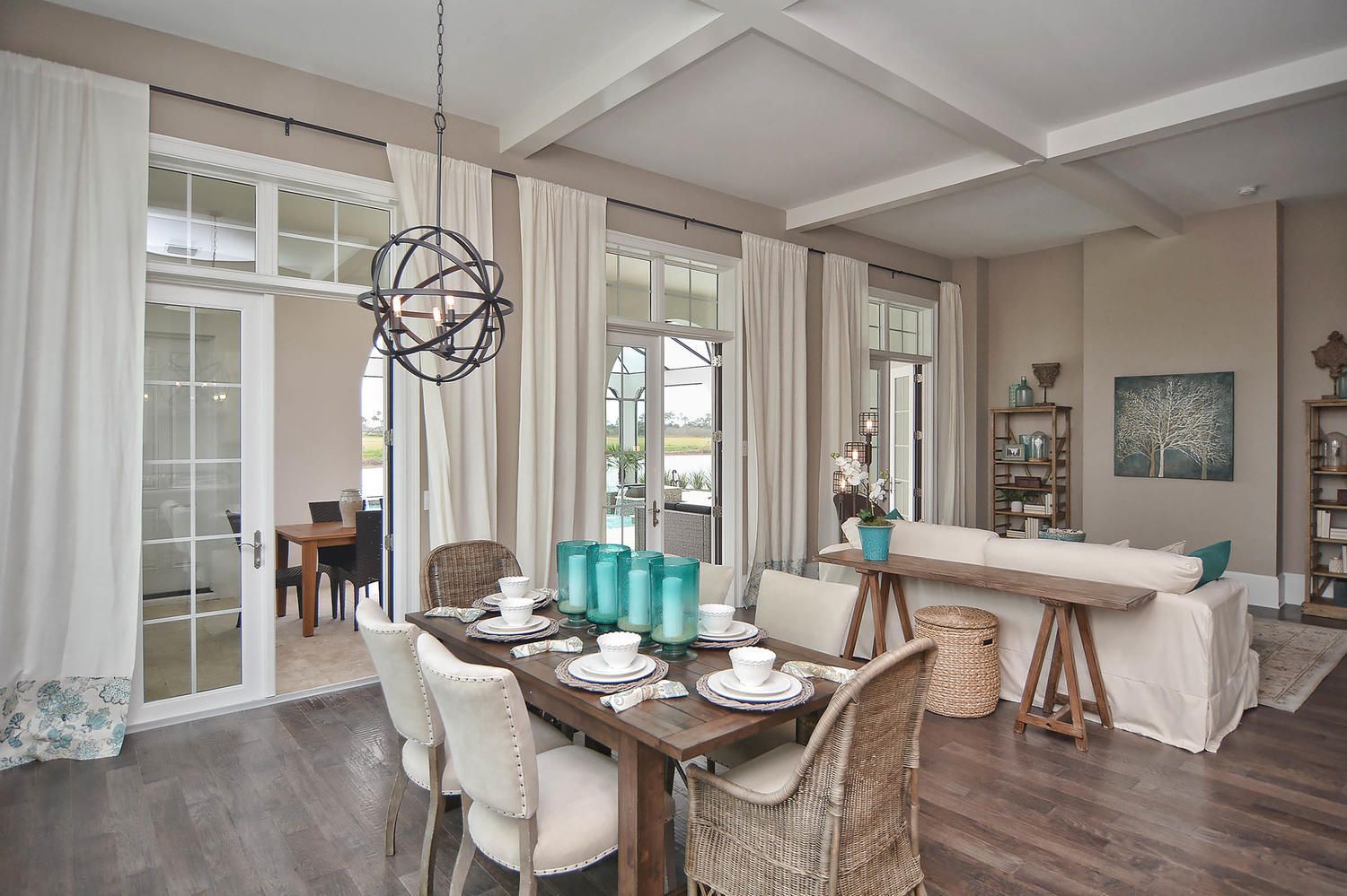 Bright open dining and living room with white curtains, wood floors, and beige furniture