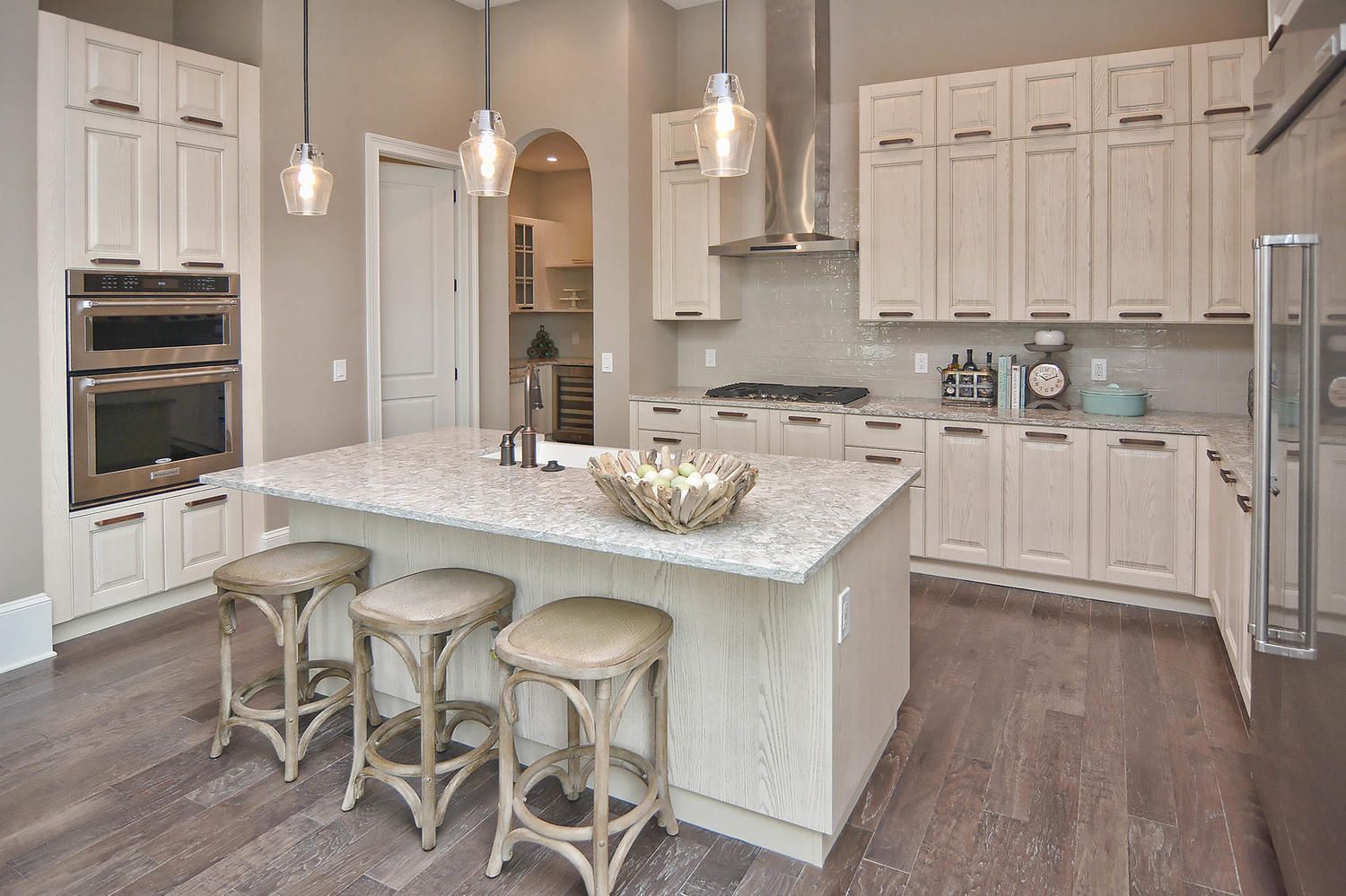 Spacious cream-colored kitchen with a large island, bar stools, pendant lights, and wood flooring