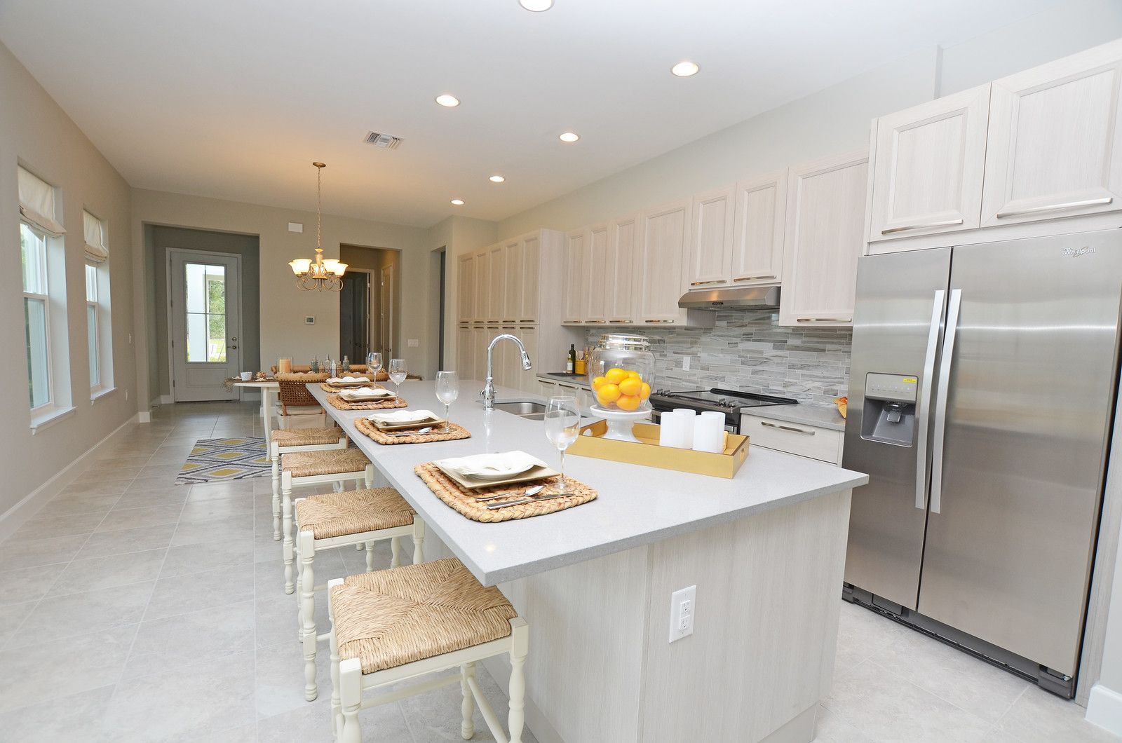 Bright modern kitchen with white cabinets, stainless fridge, island seating, and place settings on the counter
