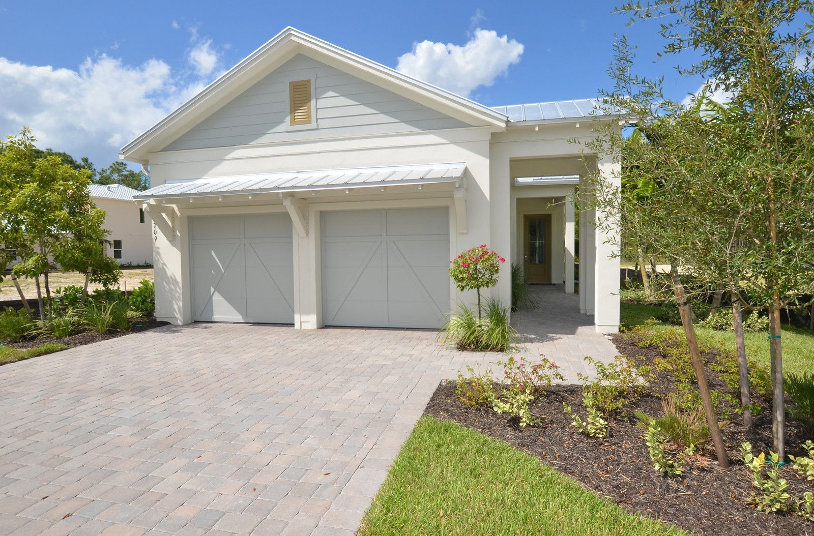 White single-story house with two-car garage, paver driveway, and landscaped front yard