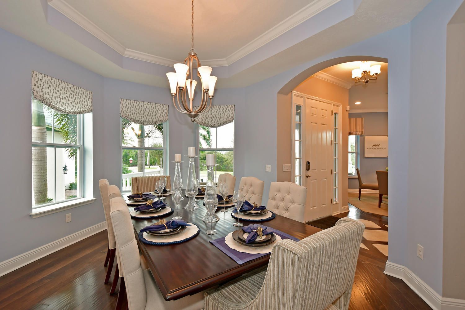 Elegant dining room with a set table, chandelier, bay windows, and arched entry to a kitchen