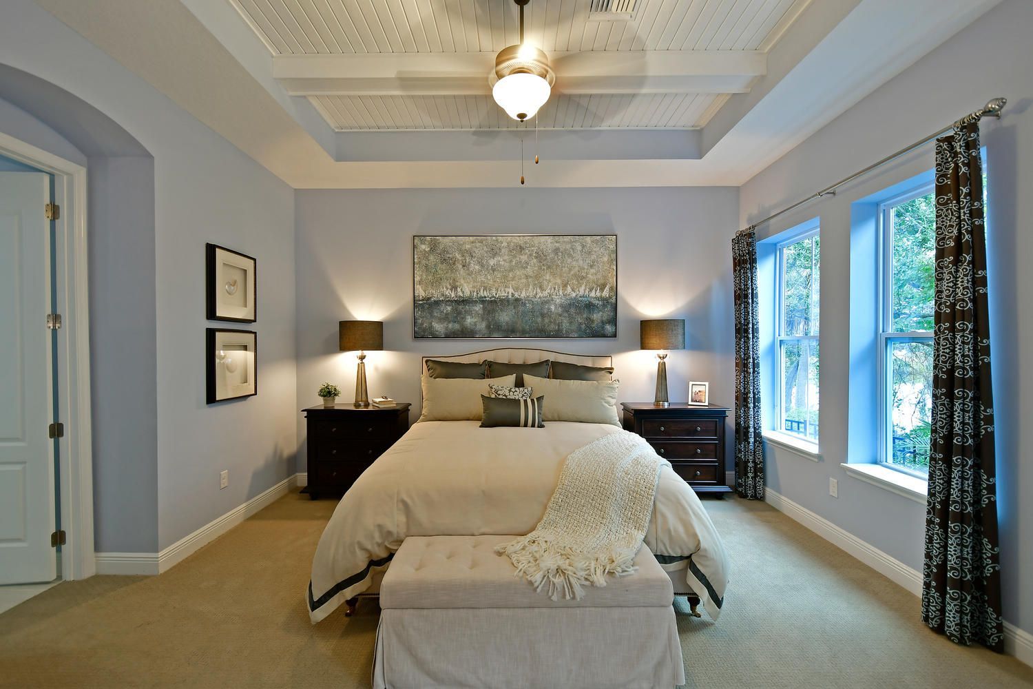 Bright bedroom with a made bed, bedside lamps, and windows with dark curtains