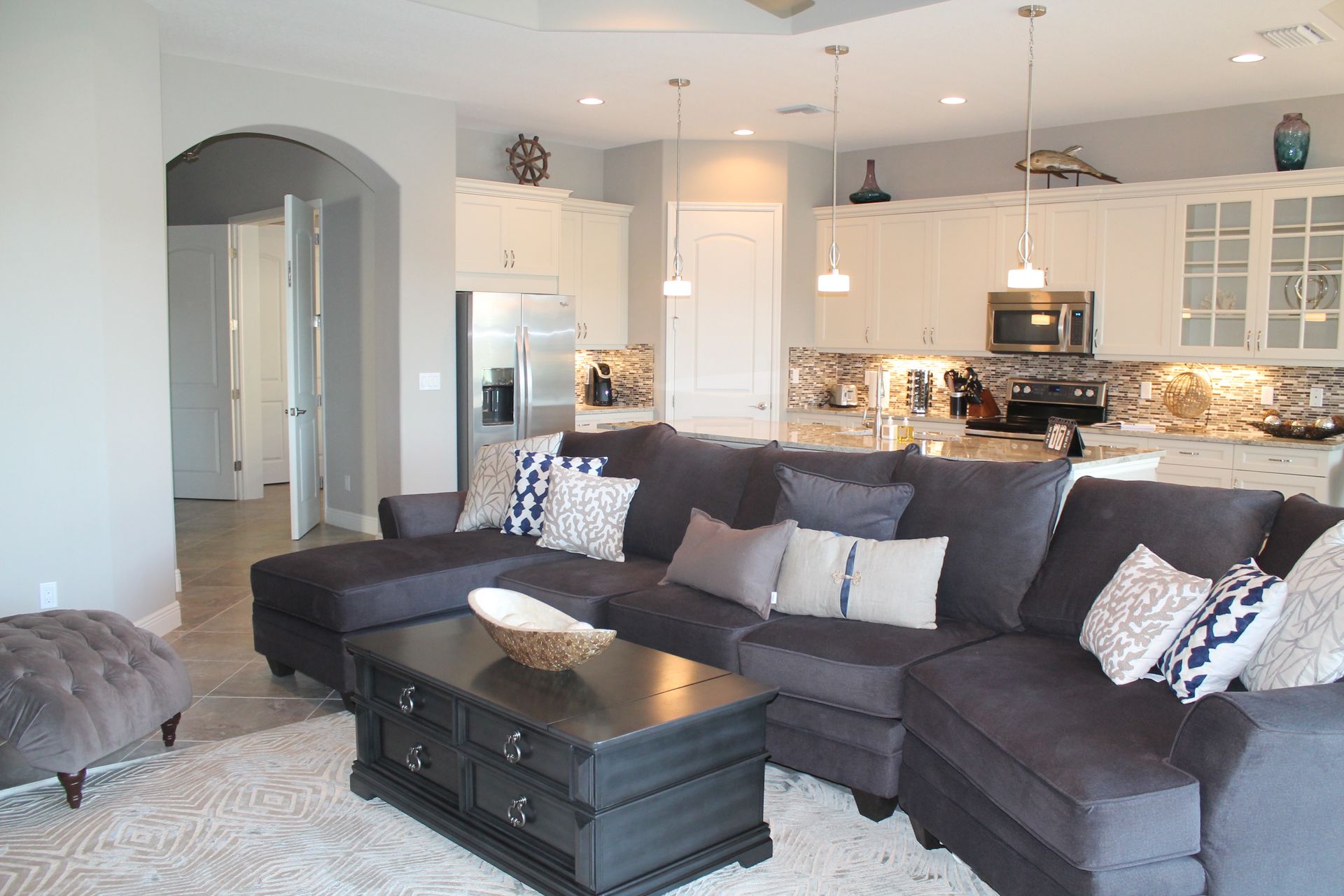 Modern open-plan living room with dark sectional sofa, white kitchen, and arched doorway
