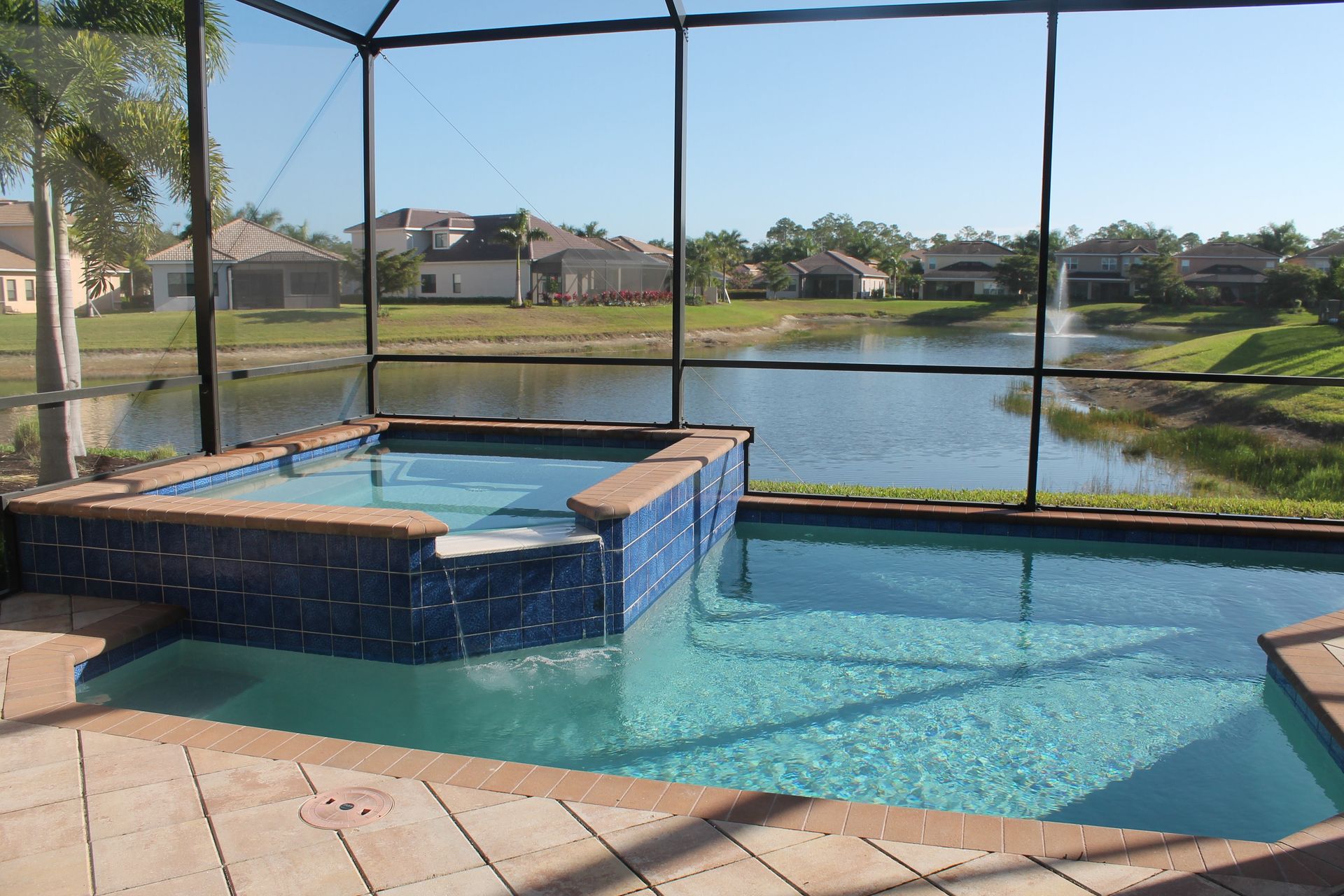 Screened backyard pool and spa overlooking a lake on a sunny day