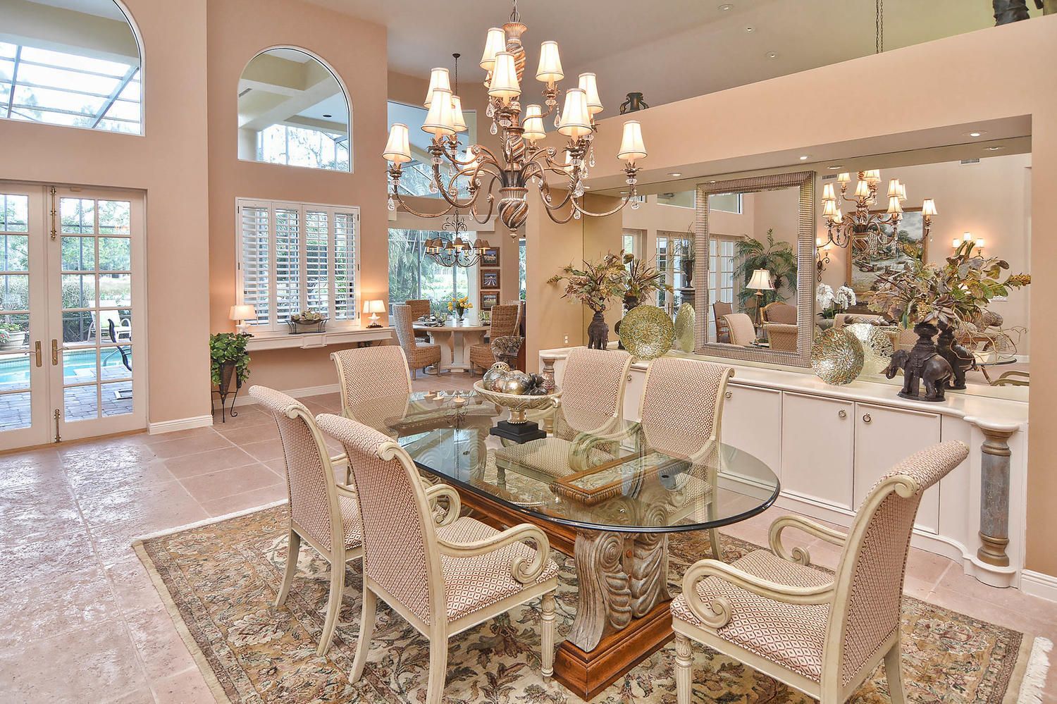 Elegant dining room with glass table, cream chairs, chandelier, and large windows